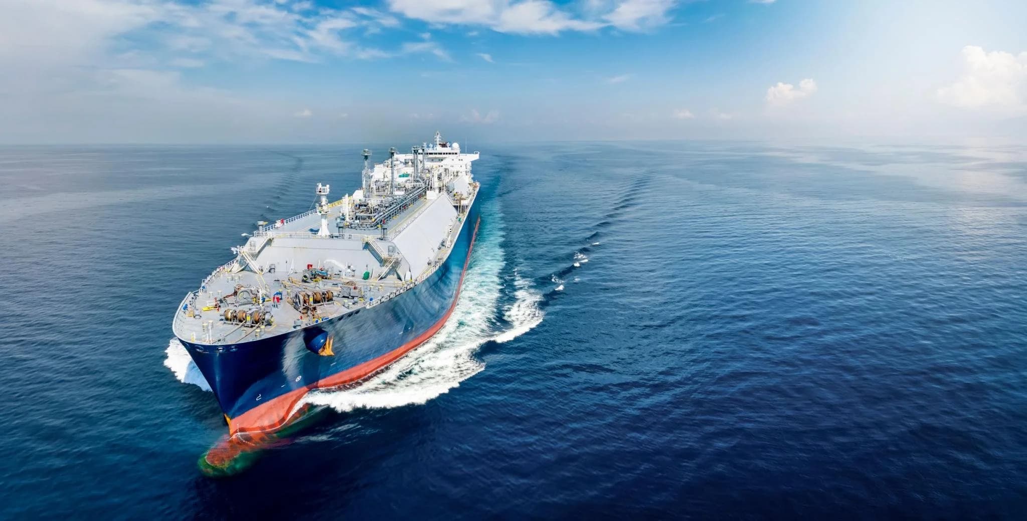 A large white and blue cargo ship sailing on calm ocean waters under a partly cloudy sky.